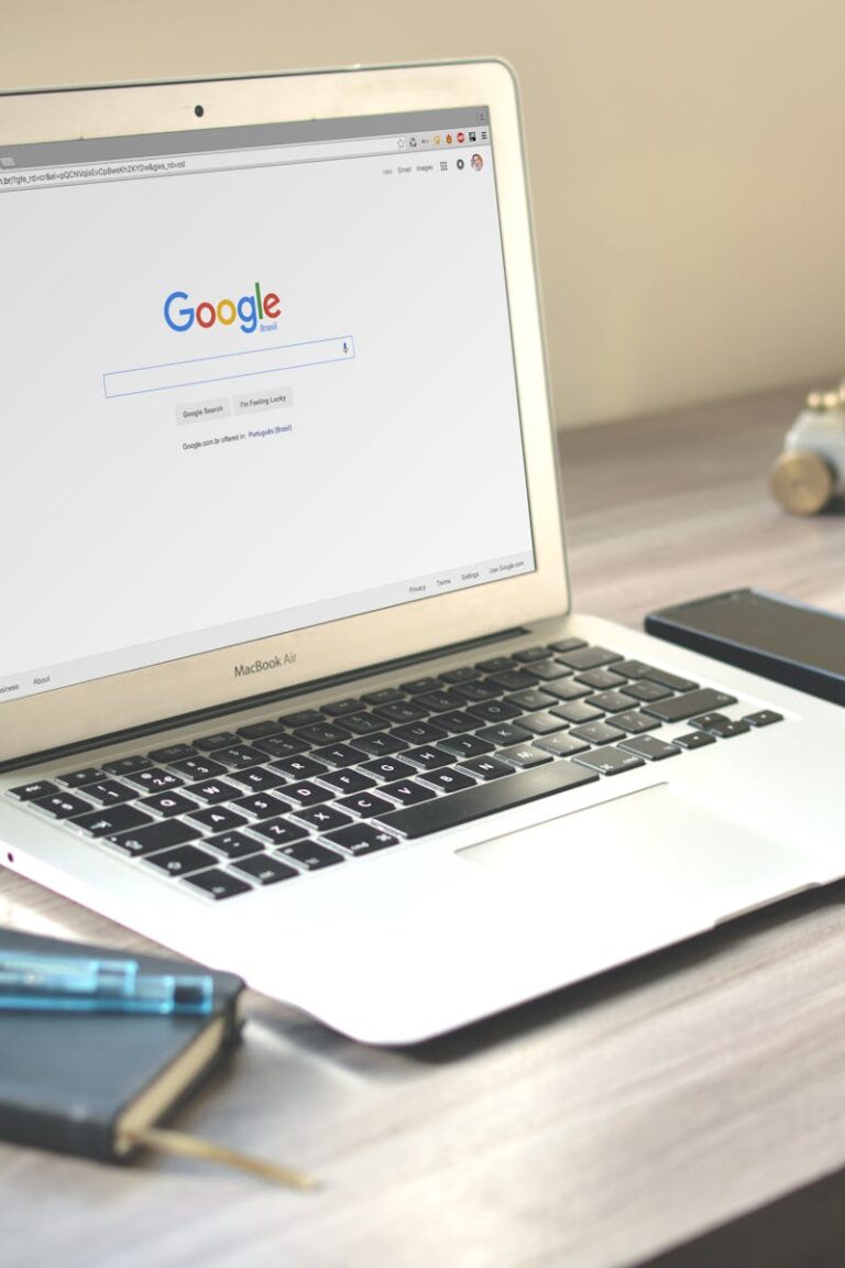 A neat workspace featuring a laptop displaying Google search, a smartphone, and a notebook on a wooden desk.